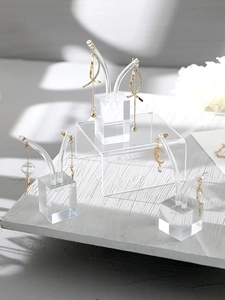 Clear acrylic jewelry stands showcasing gold tassel earrings on a white floral background