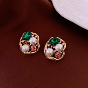 Close-up of vintage earrings with green stones and pearls on a red satin fabric