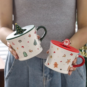 Close-up of ceramic Christmas mugs with 3D Santa and tree lids held by hand