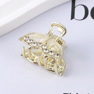 Macro shot of gold metal hair claw with rhinestones and white cat-eye leaf accents