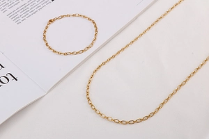 Detailed flat lay of a minimalist gold link chain necklace and bracelet set on a magazine