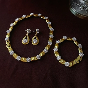 Detail of vintage matte gold jewelry set with white pearl flower clusters on dark fabric