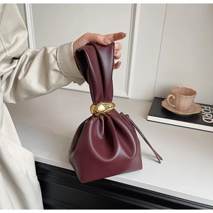 Close-up of wine red bucket bag featuring pleated design and polished gold metal handle