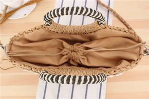 Detail of straw handbag featuring natural shells and woven handles on a wooden table