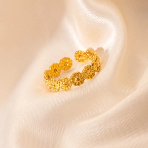 Close-up of golden daisy chain ring on beige silk background with soft lighting