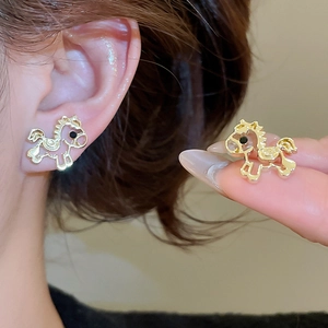 Detail of gold-tone hollow horse stud earrings with black accent and smooth metal texture
