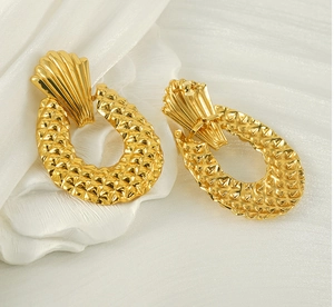 Gros plan de boucles d'oreilles dorées avec texture ananas sur fond de soie blanche