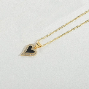 Detail of a gold heart necklace with black enamel center and sparkling zircon stones