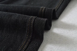 Dettaglio del tessuto denim nero con doppie cuciture a contrasto arancioni rifinite