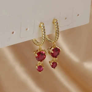 Macro detail of gold hoop earrings featuring deep red circular zircons on silk background