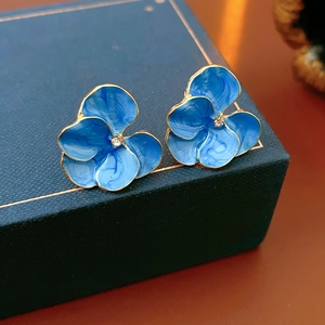 Détail macro de boucles d'oreilles fleur en émail bleu avec zircon central brillant