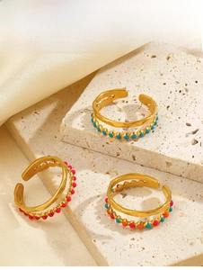 Detailed view of layered gold open rings with colorful enamel beads on a stone surface