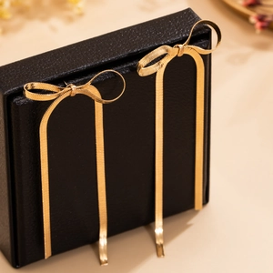Detail of long gold bow earrings with hanging snake chains on a black jewelry box