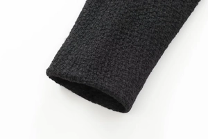 Close-up of black woven tweed jacket sleeve texture with detailed cross-stitch fabric