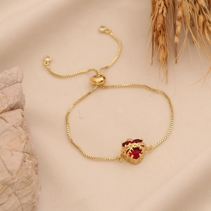 Golden heart bracelet with red gemstone on warm fabric and stone background