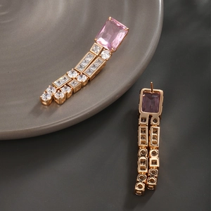 Detailed macro view of pink rectangular gemstones and sparkling zircon tassels on gold earrings