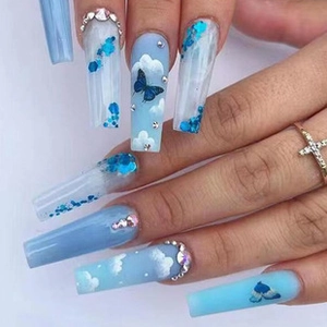 Macro shot of long coffin nails with blue cloud patterns and butterfly rhinestones