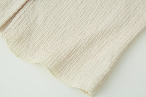 Macro shot of beige crinkled fabric texture with detailed pleats on a long sleeve suit