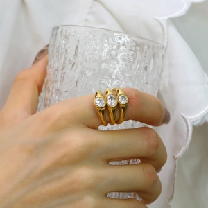 Close-up of three-layered gold rings with oval zircons worn on hand holding a glass