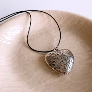 Macro view of vintage silver heart pendant with embossed floral patterns on wax cord
