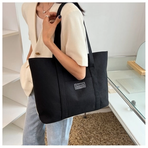 Detail of a black canvas tote bag showing the fashion label and sturdy double straps