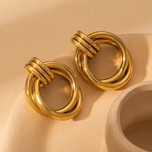 Macro detail of three-ring interlocking golden earrings on textured ceramic surface