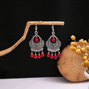 Detail of silver bohemian dangle earrings with red beads on a wooden display stand