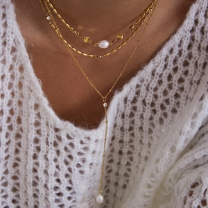 Close-up of layered gold titanium steel necklaces with pearls and cross on white knitwear