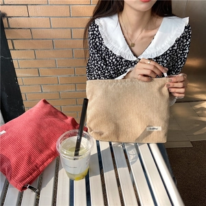 Close-up of beige corduroy pouch held by model with a red pouch in a natural setting