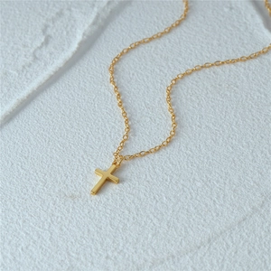 Macro shot of minimalist gold cross pendant on a fine chain over textured white stone