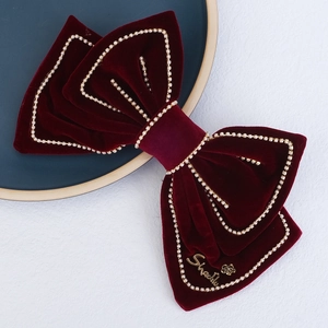 Large red velvet bow hair clip with gold bead trim on a blue decorative plate