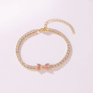 Detail view of a gold-tone tennis bracelet featuring pink heart-shaped cubic zirconia.