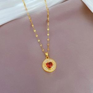 Détail d'un collier doré avec pendentif cœur rouge serti de zircons étincelants