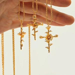 Three gold cross necklaces with unique floral designs held against a white background