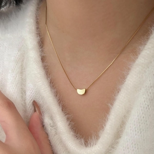 Close-up of a minimalist gold bean pendant necklace on a soft white sweater texture