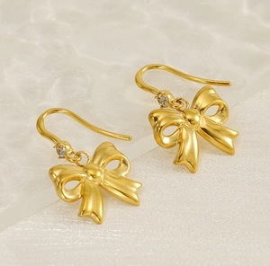 Detail of gold bow earrings with matte finish and sparkling zircon stones on a soft background