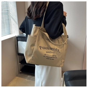 Model showing a large beige canvas tote bag with black typography in a lifestyle setting