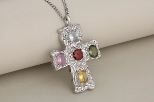 Macro shot of silver hammer-textured cross pendant with colorful oval zircon gemstones
