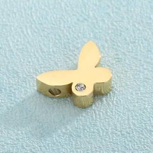 Macro detail of a golden butterfly pendant with clear gemstone and threading hole