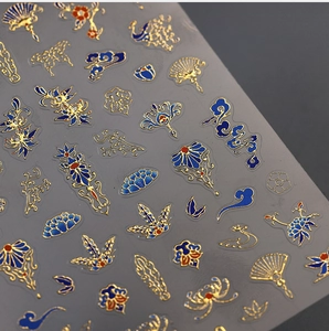 Détail macro de stickers à ongles dorés et bleu marine aux motifs de lotus et nuages
