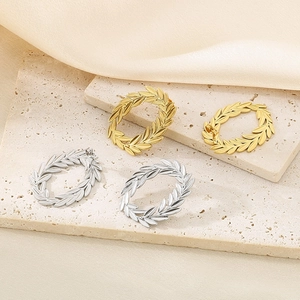 Macro detail of 18k gold and silver laurel leaf hoop earrings on textured beige stone