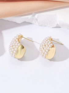 Detailed close-up of golden teardrop earrings with white pearls on a satin background
