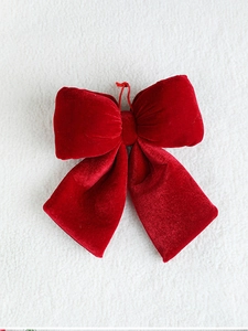 Close-up of red velvet Christmas bow with hanging rope on white textured background