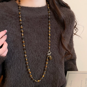 Collana di perle occhio di tigre con chiusura a T dorata su un maglione marrone scuro