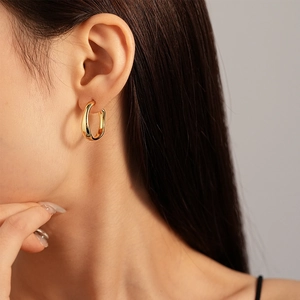 Détail de boucles d'oreilles créoles ovales dorées minimalistes portées par un mannequin