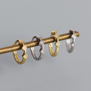 Close-up of gold and silver geometric diamond-encrusted rhombic hoop earrings on a rod