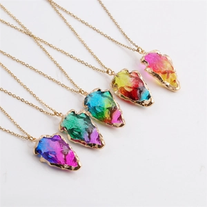 Detail of colorful crystal arrow pendants on gold chains arranged on white background
