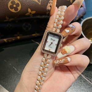 Detailed close-up of a rectangular quartz watch with shell dial and pearl bracelet strap