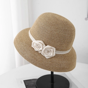 Gros plan d'un chapeau de paille kaki avec ruban crème et roses en tissu sur support