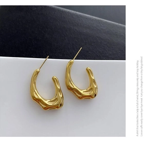 Dettaglio di orecchini a cerchio in oro a forma di C con texture lavica irregolare